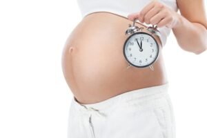 As etapas do parto normal, grávida segura um relógio despertador com a barriga de fora
