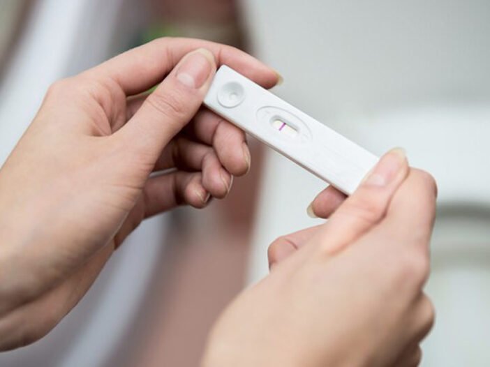Duas mãos femininas segurando um teste de gravidez de farmácia