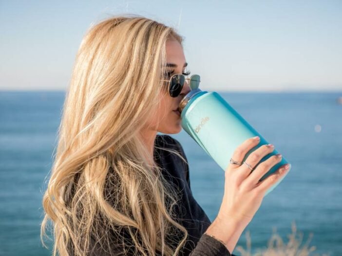 Jovem mulher bebendo a quantidade de água necessária num copo térmico turquesa