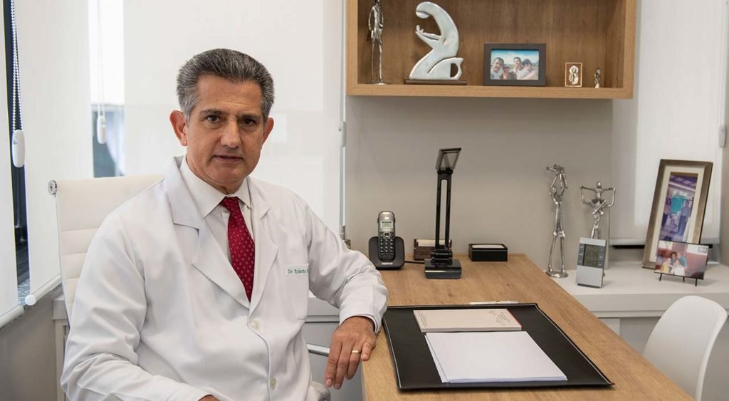 Dr Roberto Faria sentado à mesa de seu consultório